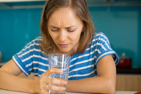 A woman in a striped shirt looks intently at a glass of water in her hands, with a thoughtful expression.