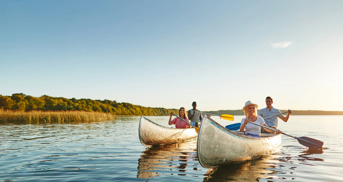 Two canoes on a lake with four people paddling under a clear sky.