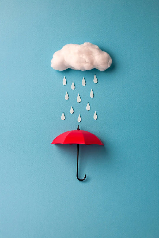 A small red umbrella shields against rain droplets falling from a fluffy white cloud against a light blue background.